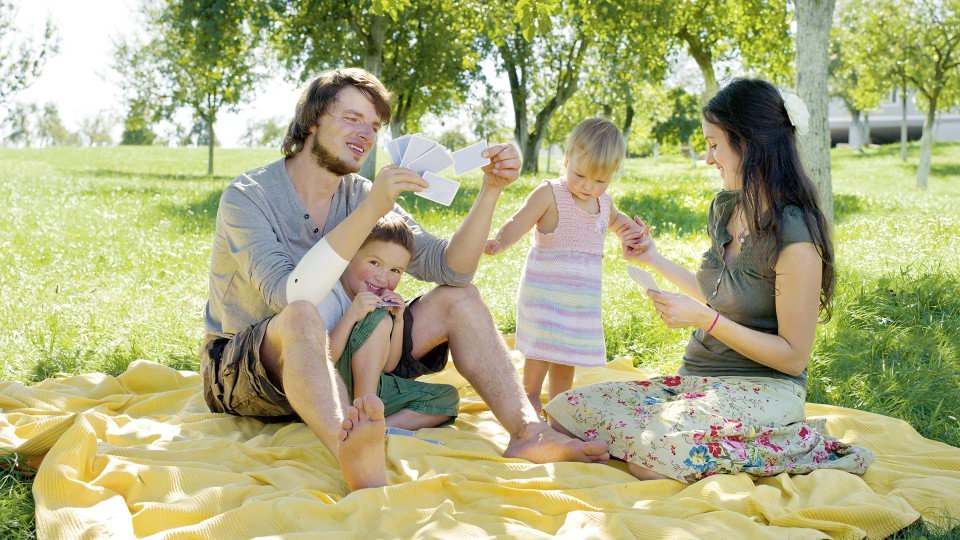 Markus with Michelangelo hand prosthesis holding his baby while playing cards with his family.